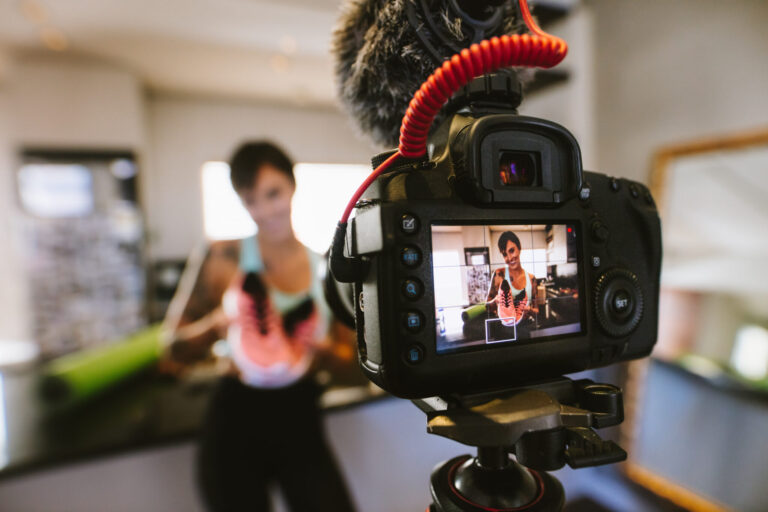 lifi media production, social media video, Female vlogger holding sports shoes in hands happily looking in camera while recording video for blog. Focus on camera with social media influencer reviewing and marketing a sports shoe.