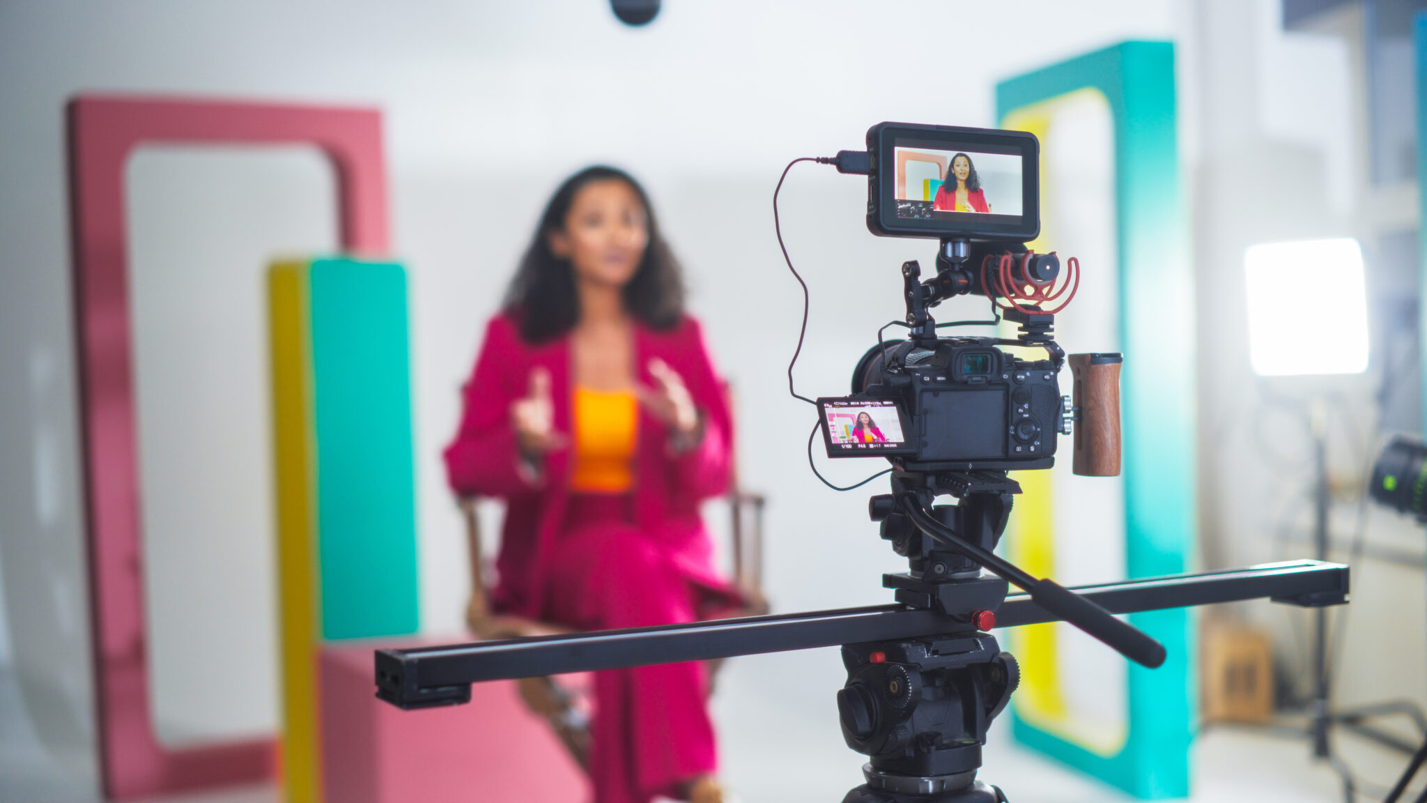 LiFi Media Production testimonial video production with a black female host in a pink suit engaging in a lively discussion on a professional set with colorful modern backdrop